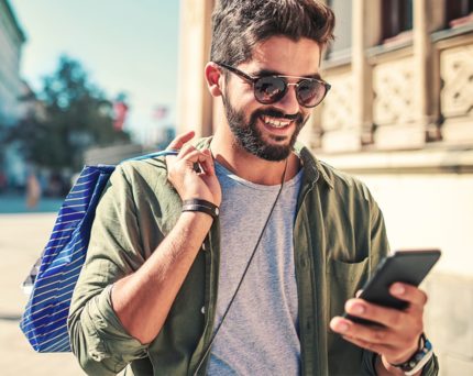 man walking outside wearing sunglasses and holding shopping bag and phone